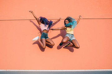 Two young beautiful black women outdoor jumping spreading arms having fun