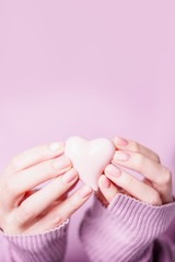 Beautiful female hands holding pink heart on the pale violet pink background. Manicure with pink color nail polish, nude manicure with fern pattern