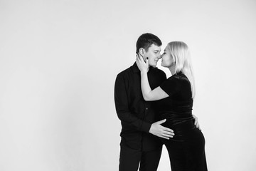 Pregnant woman and her husband hugging and holding onto your stomach in black clothes on a white background. Black and white picture. Beautiful married couple. Copy, empty space for text