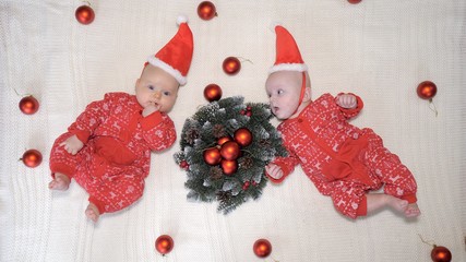 Twin Babies In Christmas Hats Lying Together On Knit Blanket. Xmas Concept.