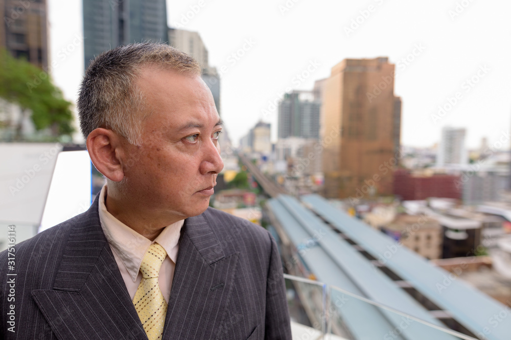 Wall mural Portrait of mature Asian businessman against view of the city