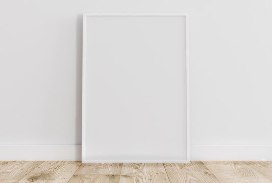 Blank vertical white poster frame standing on light wooden floor with next to white wall. Blank poster frame mockup. Empty picture frame mockup. Vertical frame mock up. Blank photo frame. 3d rendering