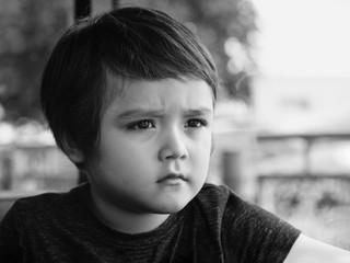 Black and white photo of lost kid looking out with worrying, Candid shot unhappy child sitting...