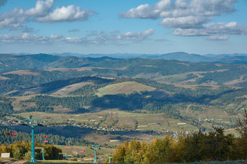 Fototapeta na wymiar Mountain landscape in Carpathian Mountains, Pylypets, Ukraine. View of the valley and village of Pylypets from Gymba Mountain. Pylons of mountain chairlift on Mount Hymba.