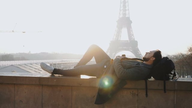 Happy male tourist lying down to relax at epic sunset Eiffel Tower view in Paris during autumn vacation slow motion.