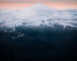 Beautiful landscape view of snowy Ben Nevis with dramatic clouds above the peak during sunrise.