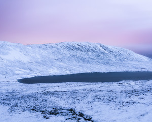 Pink sky, white mountain, frozen lake, a snow coated long-exposure landscape view on Ben Nevis during winter sunrise