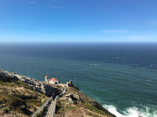 Steep stairs lead down a rocky path to the Point Reyes lighthouse with the Pacific Ocean in the...