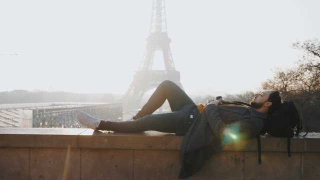 Relaxed happy male tourist lying down with eyes closed at amazing sunset Eiffel Tower view in Paris slow motion.