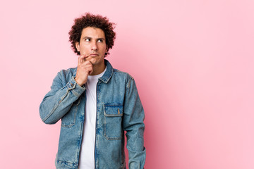Fototapeta na wymiar Curly mature man wearing a denim jacket against pink background looking sideways with doubtful and skeptical expression.