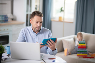 Bearded man in a blue shirt looking concentrated looking at the tablet