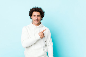 Young sporty man against a blue background smiling and pointing aside, showing something at blank space.