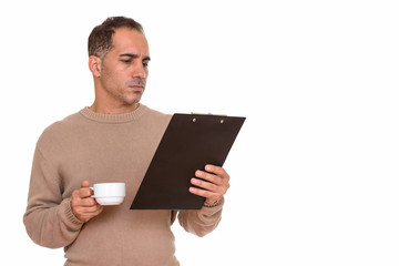 Mature handsome Persian man drinking coffee while reading on clipboard