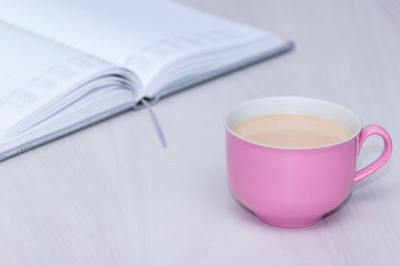 Obraz na płótnie Canvas Pink cup of coffee, open notebook on wooden desk table. Freelancer or bloger, copywriter concept.