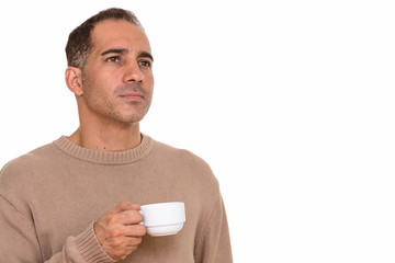 Mature handsome Persian man holding coffee cup while thinking