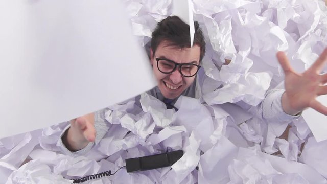 malicious man office worker in glasses cries in a large heaps of crumpled paper slow mo