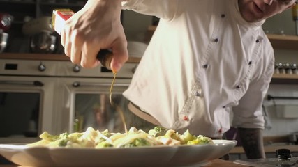 chef in modern kitchen pours olive oil on pasta with fish and spaghetti from bottle. Gastronomy culinary. utensil in the kitchen. Delicious dinner at home or in restaurant. - Powered by Adobe