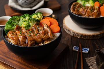 Japanese Food Style : Homemade Chicken Teriyaki grilled with rice , carrot , broccoli put on the black bowl and place on wooden table
