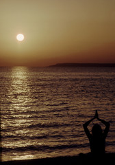 silhouette of woman doing yoga on beach at sunset