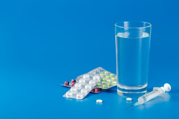 Glass with water, pills, syringe on blue background with copy space