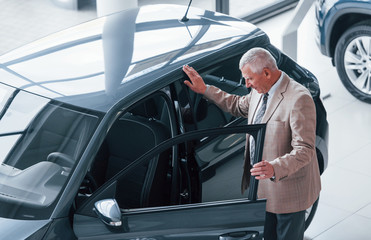 Naklejka premium Aged man in formal wear walking in the automobile salon and looking for the car