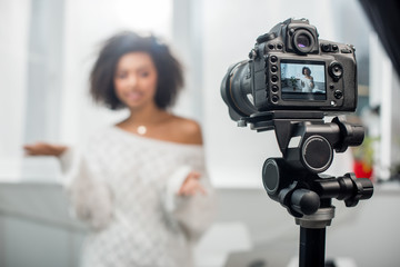 Naklejka premium selective focus of digital camera with attractive african american influencer gesturing while talking on display