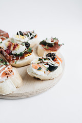 Delicious fresh bruschettas with eggs, salmon, olives and meat , traditional Italian cuisine, ingredients on white  table