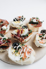 Delicious fresh bruschettas with eggs, salmon, olives and meat , traditional Italian cuisine, ingredients on white  table
