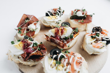 Delicious fresh bruschettas with eggs, salmon, olives and meat , traditional Italian cuisine, ingredients on white  table