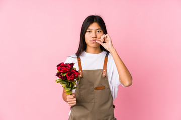 Young chinese gardener woman holding a roses isolated with fingers on lips keeping a secret.