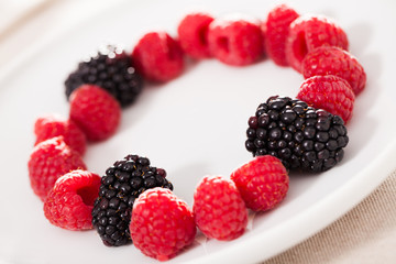 raspberries and blackberries laid out on a white plate in circle