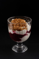 Yogurt parfait dessert with berries and granola crunch on black background