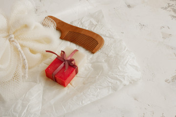 Beautifully packaged natural pink and white soap in colored ribbon, natural loofah and wooden hair comb with cloves on a light decorative background. Natural self care concept. Selective focus