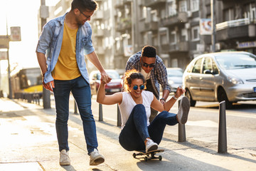 Group of friends hangout at the city street.Female sitting on skate board while friends pushing her from behind.	