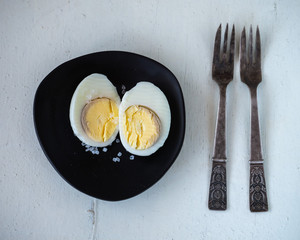 Boiled chicken egg cut into two halves and coarse salt on a black plate