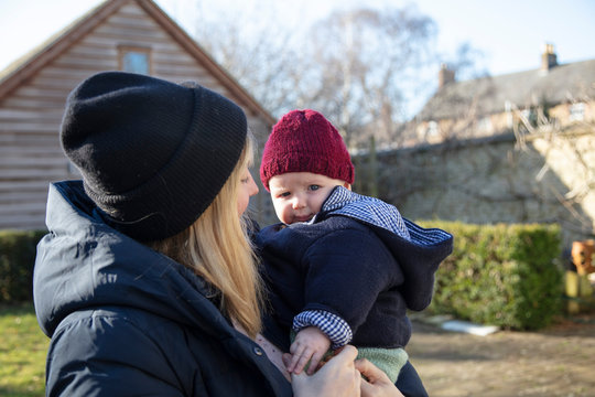 Happy Mother Holding Baby Son In Her Arms During Winter