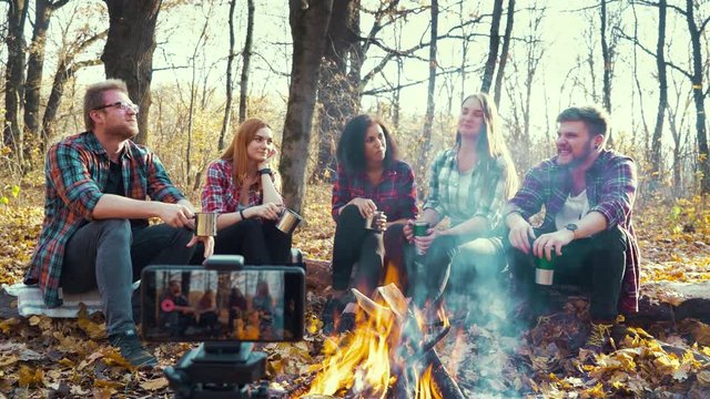 Travel bloggers sitting by campfire and streaming for social media