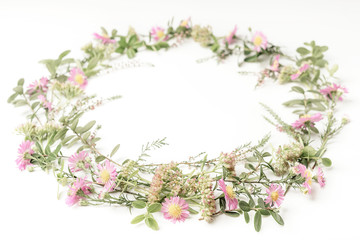 Beautiful and tender wreath frame with pink flowers, heath, branches and leaves on white background. Top view. Copy space.