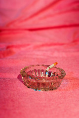 Ashtray with burning cigarette on sunbed with pink towel.