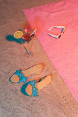 Vintage blue ladies shoes and cocktail next to pink towel with sunglasses on it.