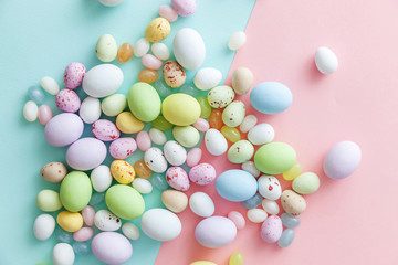 Happy Easter concept. Preparation for holiday. Easter candy chocolate eggs and jellybean sweets isolated on trendy pastel blue pink background. Simple minimalism flat lay top view copy space.