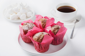 Muffins, marshmallows and black coffee on a white table.