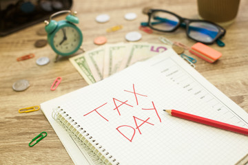 Tax day written in red into the notebook, office table background