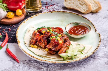 Closeup Homemade Buffalo chicken wings and chili pepper sauce, vegetables at a table background.