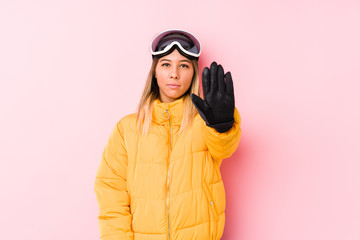 Young caucasian woman wearing a ski clothes in a pink background standing with outstretched hand showing stop sign, preventing you.