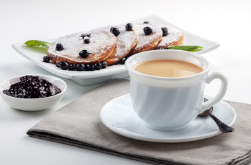 A Cup of coffee with milk and a plate with a pancakes is on the table.
