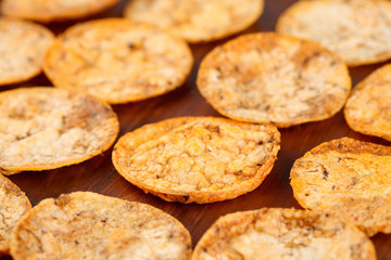 Close up of organic, crispy, baked, whole grain rice chips with tomato and paprika spices. Gluten free healthy snack on a wooden background. Selective focus and very shallow depth of field