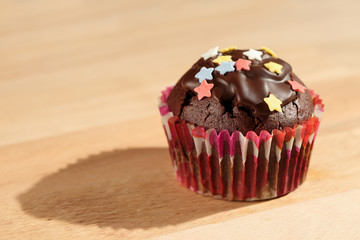 Homemade, delicious cocoa muffin with colorful sugar stars and dark chocolate icing on a wooden board. Close up, shallow depth of field and selective focus