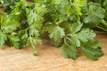 Extreme close up of fresh, garden parsley leaves on a scratched wooden cutting board with water drops and sun haze