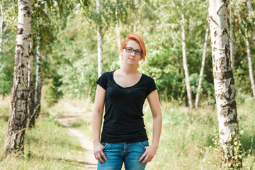Young beautiful ginger girl in black t-shirt posing in summer birch forest.